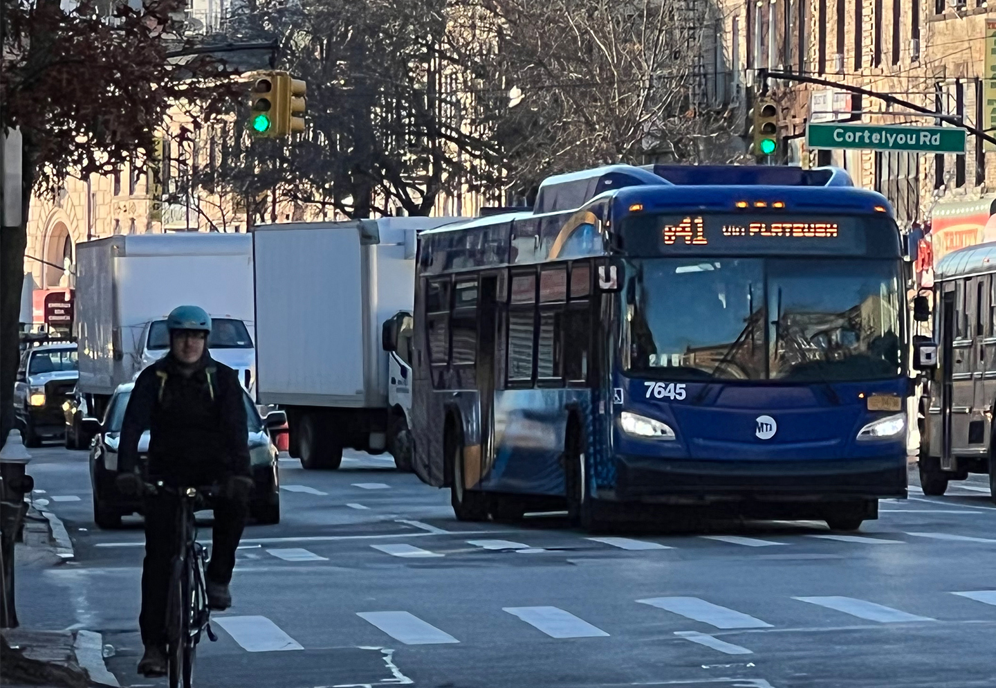 A person riding a bike and a bus in heavy traffic on a street full of cars and trucks.