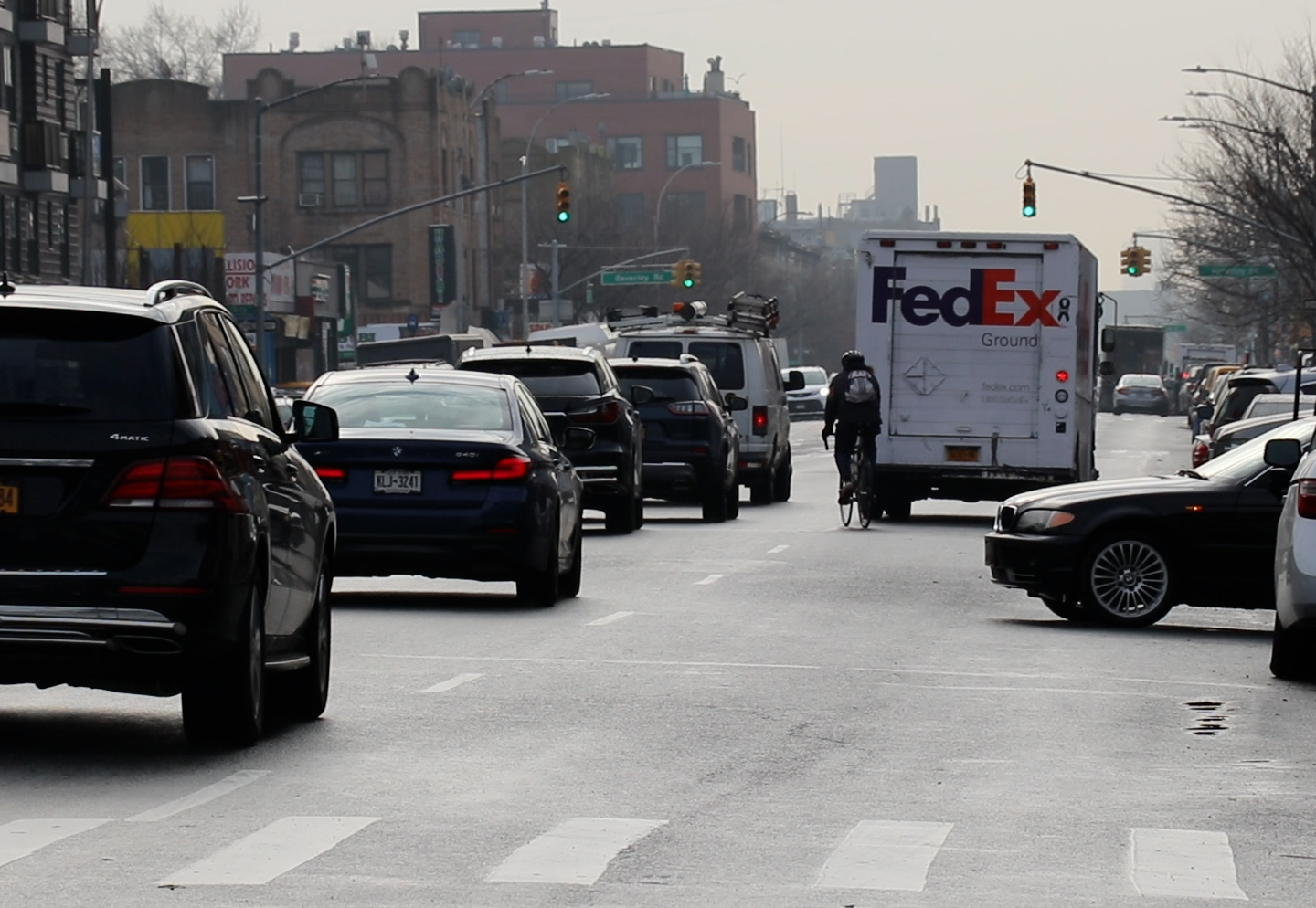 On a wide road, a cyclist merges into car traffic to pass a double-parked FedEx truck that's blocking an entire lane.