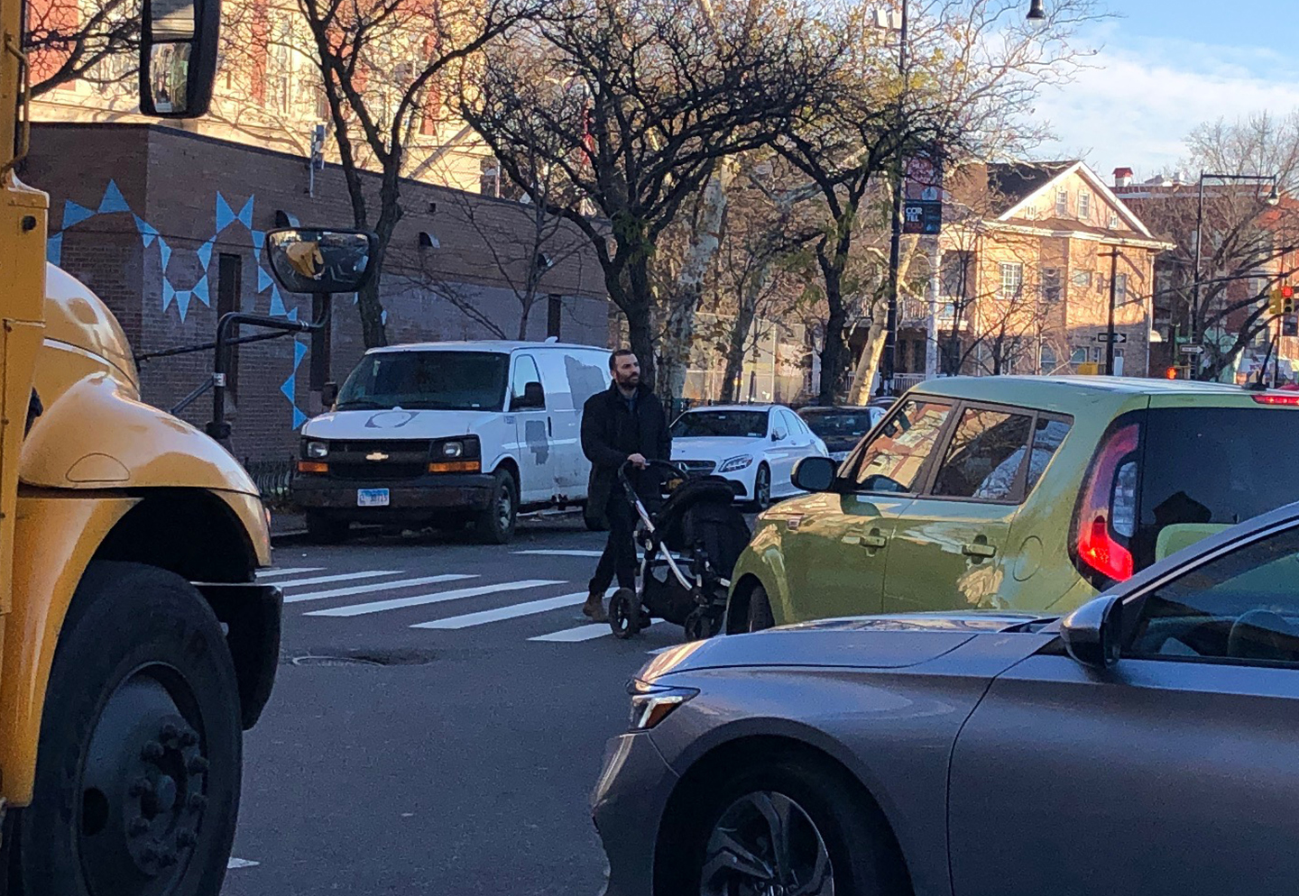 A man in a crosswalk with a stroller, with a car uncomfortably close, waiting to turn.